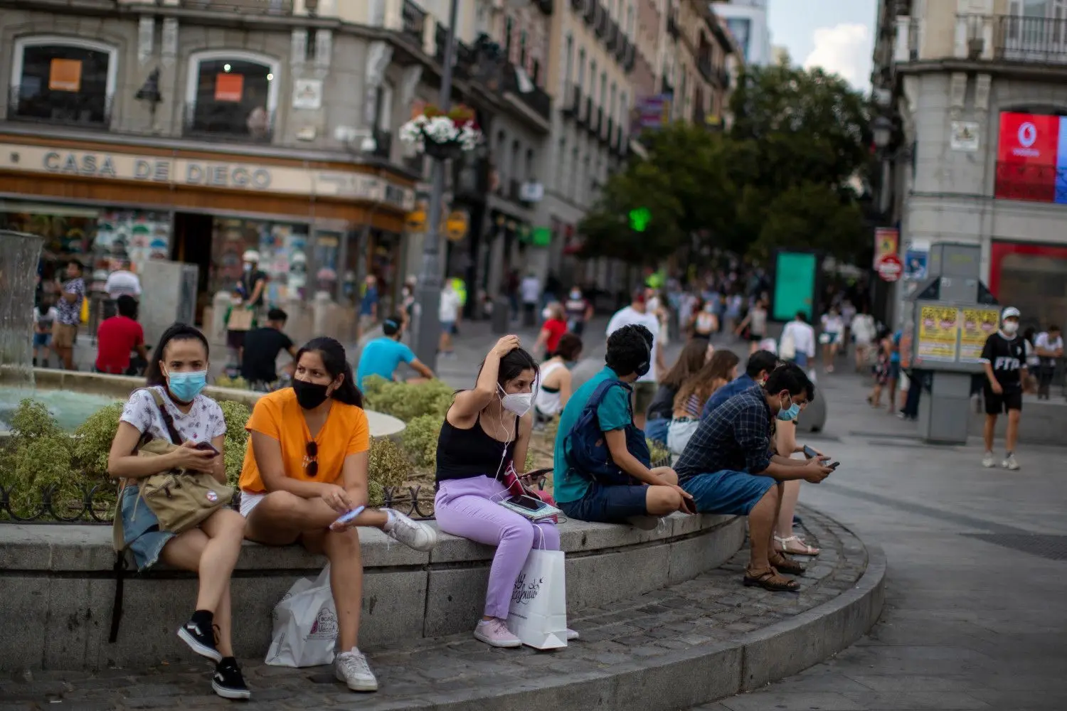 Menschen mit Masken sitzen auf einer Straßenbank in Madrid. Das Auswärtige Amt warnt wegen der Corona-Pandemie nun auch vor Reisen in Spaniens Hauptstadt und ins spanische Baskenland.