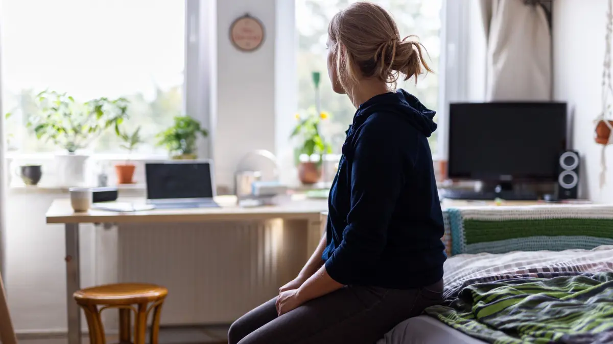Eine Studentin sitzt auf dem Bett in ihrem WG–Zimmer: ILLUSTRATION - 13.08.2023, Niedersachsen, Hannover: Einsamkeit betrifft zunehmend auch jüngere Erwachsene und Menschen, die nicht allein leben, wie eine aktuelle Studie zeigt. (zu dpa: «Familienministerin Paus stellt Daten zu Einsamkeit in Deutschland vor») Foto: Michael Matthey/dpa +++ dpa-Bildfunk +++