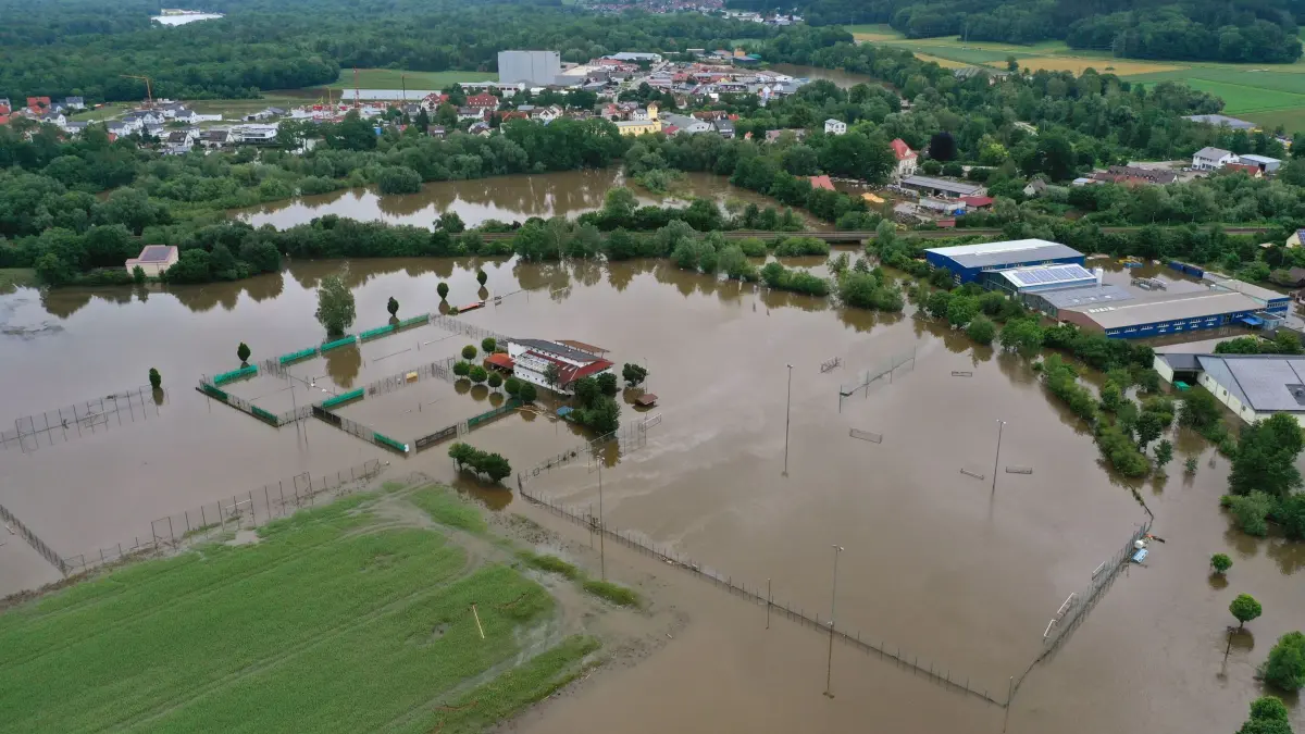 Hochwasser in Bayern — Offingen: 03.06.2024, Bayern, Offingen: Sportanlagen sind vom Hochwasser der Mindel überflutet (Luftaufnahme mit einer Drohne). Seit Tagen kämpfen die Helfer in Bayern und Baden-Württemberg gegen die Flut und ihre Folgen. Die Hochwasserlage ist weiter dynamisch und unübersichtlich. Viele kleine Gemeinden sind betroffen, mancherorts spitzt sie sich die Lage sogar zu. Foto: Karl-Josef Hildenbrand/dpa +++ dpa-Bildfunk +++