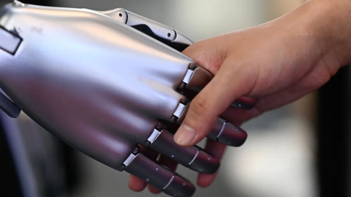 A man shakes hands with a Tesla humanoid robot on display during the World Intelligence Expo in Tianjin on June 23, 2024. (Photo by Pedro PARDO / AFP)