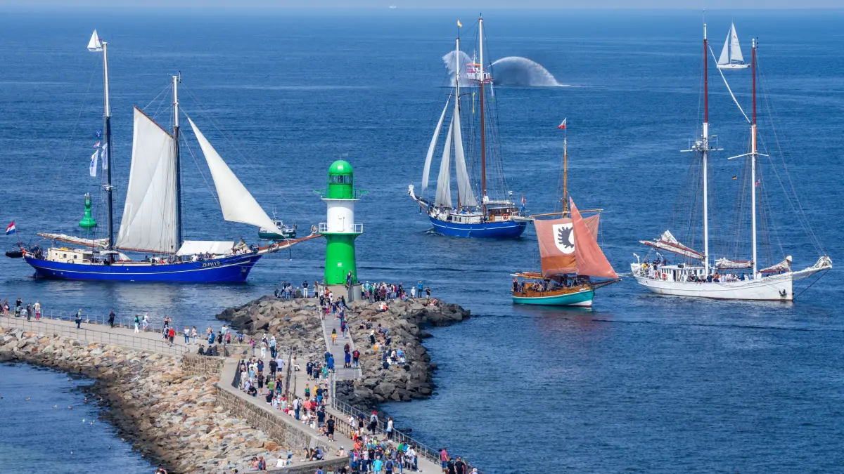 Bei der Hanse Sail kreuzen historische Segelschiffe auf der Ostsee vor dem Hafen von Warnemünde und passieren die Leuchtfeuer auf den Molenköpfen.