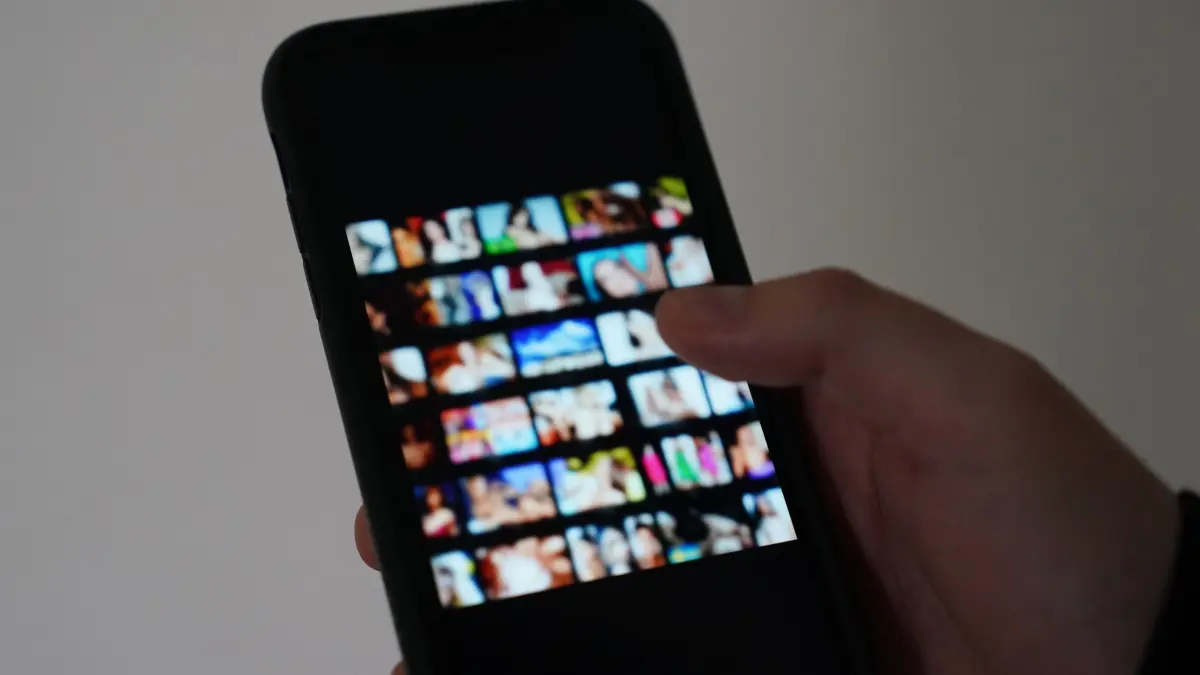 ARCHIV - Ein Mann schaut sich auf einem Smartphone eine Porno-Internetseite an (gestellte Szene). Es beginnt mit einem vermeintlichen Online-Flirt und endet mit Geldforderungen. Sextortion wird diese Form der Erpressung genannt. Es gibt Möglichkeiten, sich davor zu schützen. (zu dpa: «Polizei warnt vor sexueller Erpressung im Internet») +++ dpa-Bildfunk +++