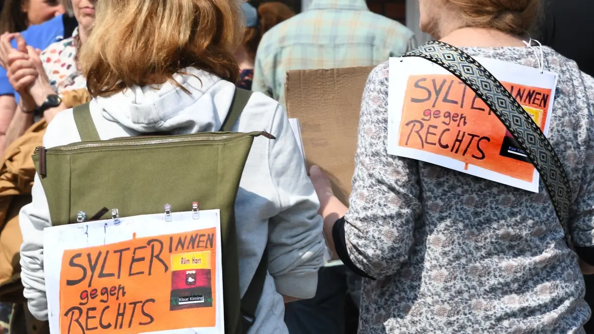 Nach Rassismus-Eklat - Mahnwache auf Sylt: ARCHIV - 26.05.2024, Schleswig-Holstein, Kampen: «Sylter gegen Rechts!» steht auf Plakaten, die zwei Frauen bei einer Mahnwache auf Sylt auf ihre Rücken geheftet haben. Im Internet hatte sich ein Videoclip aus einer Sylter Bar verbreitet, auf dem Partygäste zu einem Pop-Hit rassistische Parolen grölen. Inselbewohner protestieren mit einer Mahnwache gegen Rechts. (zu dpa: «Die wichtigsten Ereignisse des Jahres 2024 - Mai») Foto: Lea Sarah Albert/dpa +++ dpa-Bildfunk +++