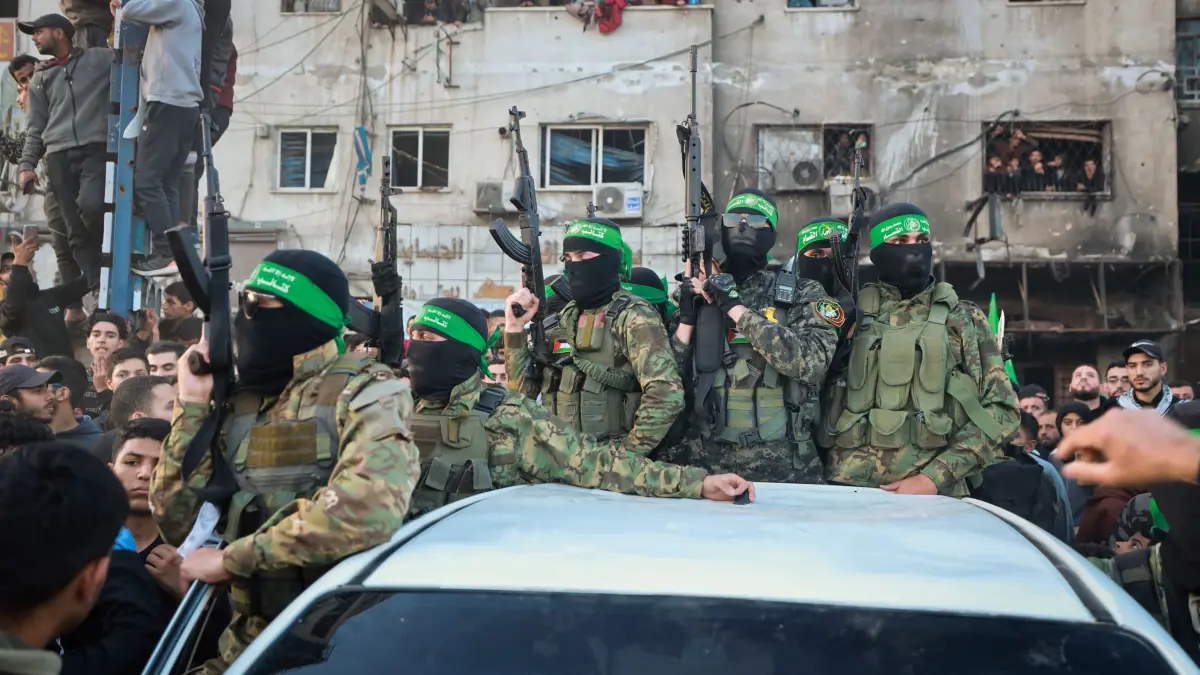 Nahostkonflikt - Gaza: 20.01.2025, Palästinensische Gebiete, Gaza-Stadt: Kämpfer der Qassam-Brigaden, des militärischen Flügels der Hamas, stehen auf einem Auto, als Fahrzeuge des Roten Kreuzes zur Abholung israelischer Geiseln, die im Rahmen eines Waffenstillstandsabkommens zwischen Israel und der Hamas freigelassen wurden, in Gaza-Stadt rangieren. Foto: Abed Hajjar/AP/dpa +++ dpa-Bildfunk +++