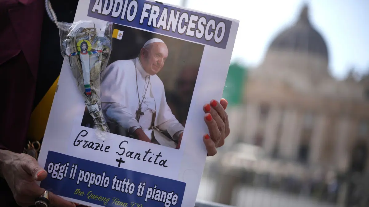 Papst Franziskus gestorben - Vatikan: 21.04.2025, Italien, Vatikanstadt: Eine Frau hält ein Bild von Papst Franziskus, auf dem in italienischer Sprache zu lesen ist: "Lebe wohl, Franziskus, danke, Seine Heiligkeit, heute weint das ganze Volk um dich" auf dem Petersplatz im Vatikan, nachdem Kardinal Camerlengo Kevin Joseph Farrell den Tod von Papst Franziskus bekannt gegeben hat. Foto: Andrew Medichini/AP/dpa +++ dpa-Bildfunk +++
