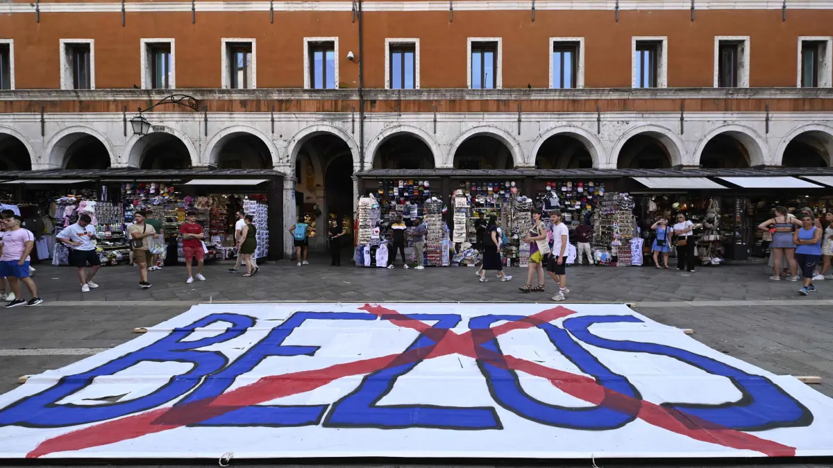 People gather to protest against the wedding of Amazon Founder and CEO Jeff Bezos and journalist Lauren Sanchez in Venice, on June 13, 2025. Poster campaigns and stickers have spread throughout the city, including one with images of Bezos reading "No space for Bezos" as some local residents protest claiming the city is transformed into a playground for billionaires. (Photo by ANDREA PATTARO / AFP)