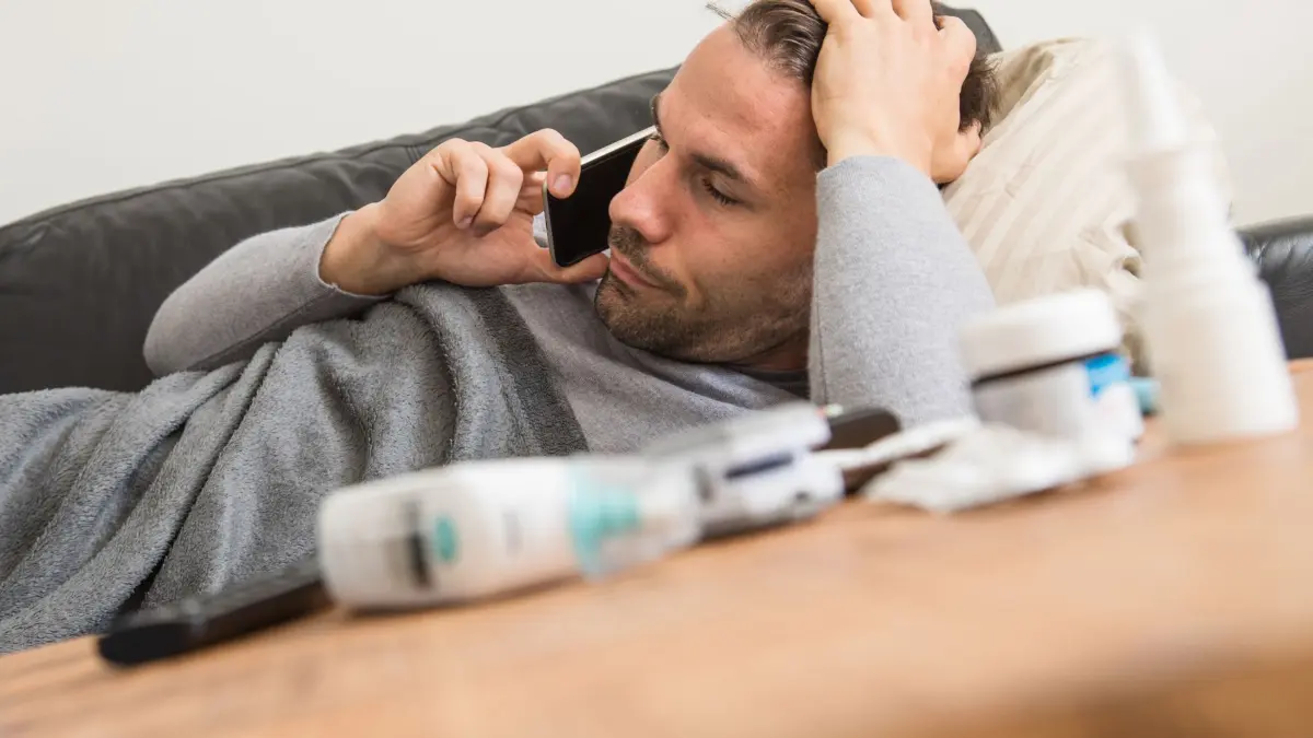Mann liegt krank auf einem Sofa und telefoniert: ILLUSTRATION - In Notfällen müssen Beschäftigte unter Umständen erreichbar sein, auch wenn sie sich krankgemeldet haben. (zu dpa: «Muss man auch im Falle einer Krankmeldung erreichbar sein?») Foto: Christin Klose/dpa-tmn - Honorarfrei nur für Bezieher des dpa-Themendienstes +++ dpa-Themendienst +++