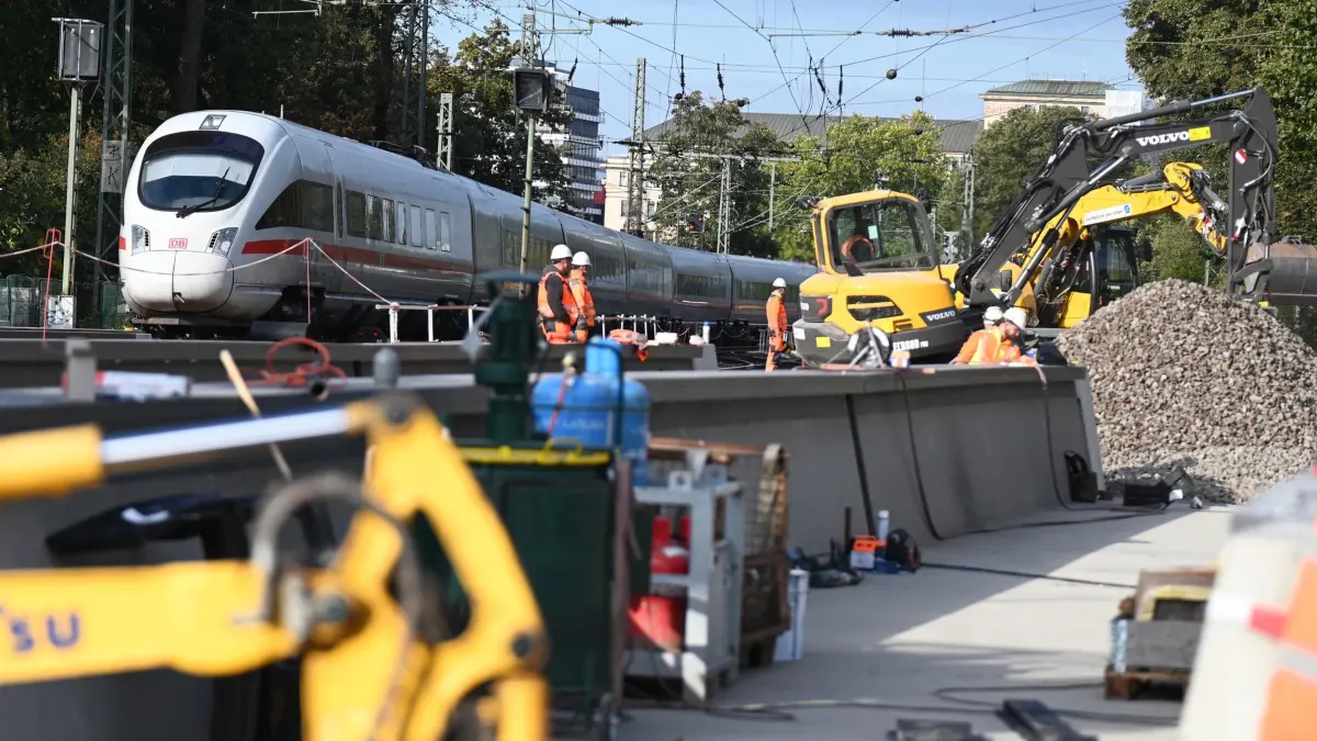 Neubau Eisenbahnbrücken Ferdinandstor in Hamburg: 30.09.2025, Hamburg: Arbeiter stehen an der Bahn-Überführung Ferdinandstor/An der Alster, neben ihnen fährt ein ICE über die Schienen. Die letzten Brückenteile der Überführung werden eingehoben, dafür haben Spezialfahrzeuge vormontierte Stahlüberbauten an ihre endgültigen Positionen gebracht. Foto: David Hammersen/dpa +++ dpa-Bildfunk +++