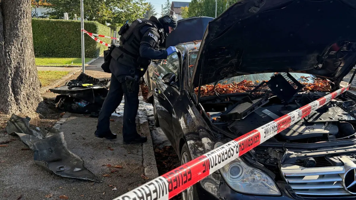 Brand in München - Großeinsatz von Polizei und Feuerwehr: 01.10.2025, Bayern, München: Ein Polizist mit Schutzweste steht an einem PKW, der gebrant hatte. Ein Brand in einem Münchner Einfamilienhaus hat einen Großeinsatz von Polizei und Feuerwehr ausgelöst. Es kam deswegen zu größeren Verkehrsbehinderungen, eine Gefahr für die Bevölkerung bestehe nicht, sagte ein Polizeisprecher am Morgen Foto: Roland Freund/dpa +++ dpa-Bildfunk +++
