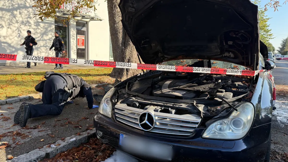 Brand in München - Großeinsatz von Polizei und Feuerwehr: 01.10.2025, Bayern, München: Ein Polizist mit Schutzweste untersucht einen PKW, der gebrannt hatte. Ein Brand in einem Münchner Einfamilienhaus hat einen Großeinsatz von Polizei und Feuerwehr ausgelöst. Es kam deswegen zu größeren Verkehrsbehinderungen, eine Gefahr für die Bevölkerung bestehe nicht, sagte ein Polizeisprecher am Morgen Foto: Roland Freund/dpa - ACHTUNG: Kennzeichen wurde(n) aus rechtlichen Gründen gepixelt +++ dpa-Bildfunk +++