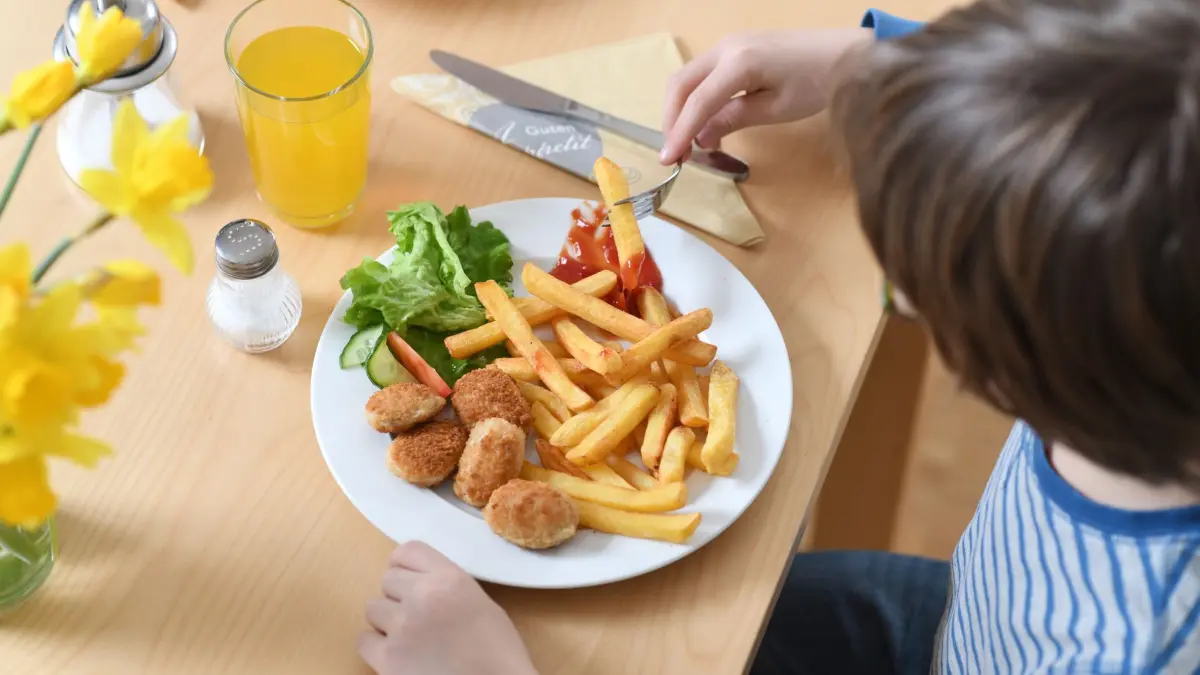 Ein Kind isst Chicken Nuggets und Pommes Frites: ILLUSTRATION - 19.03.2019, Bayern, München: Viel Pommes, wenig Auswahl: Auf den meisten Kinderspeisekarten dominieren Schnitzel, Nuggets und Nudeln. (zu dpa: «Britisches Werbeverbot für Junk-Food wird umgesetzt») Foto: Tobias Hase/dpa/dpa-tmn +++ dpa-Bildfunk +++