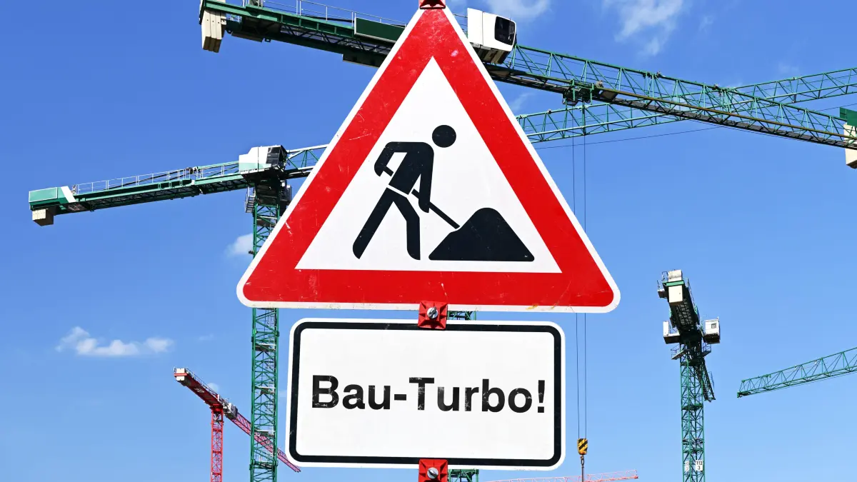 Symbolbild: Bau-Turbo: Schild mit Aufschrift Bau-Turbo vor Baukränen, Fotomontage