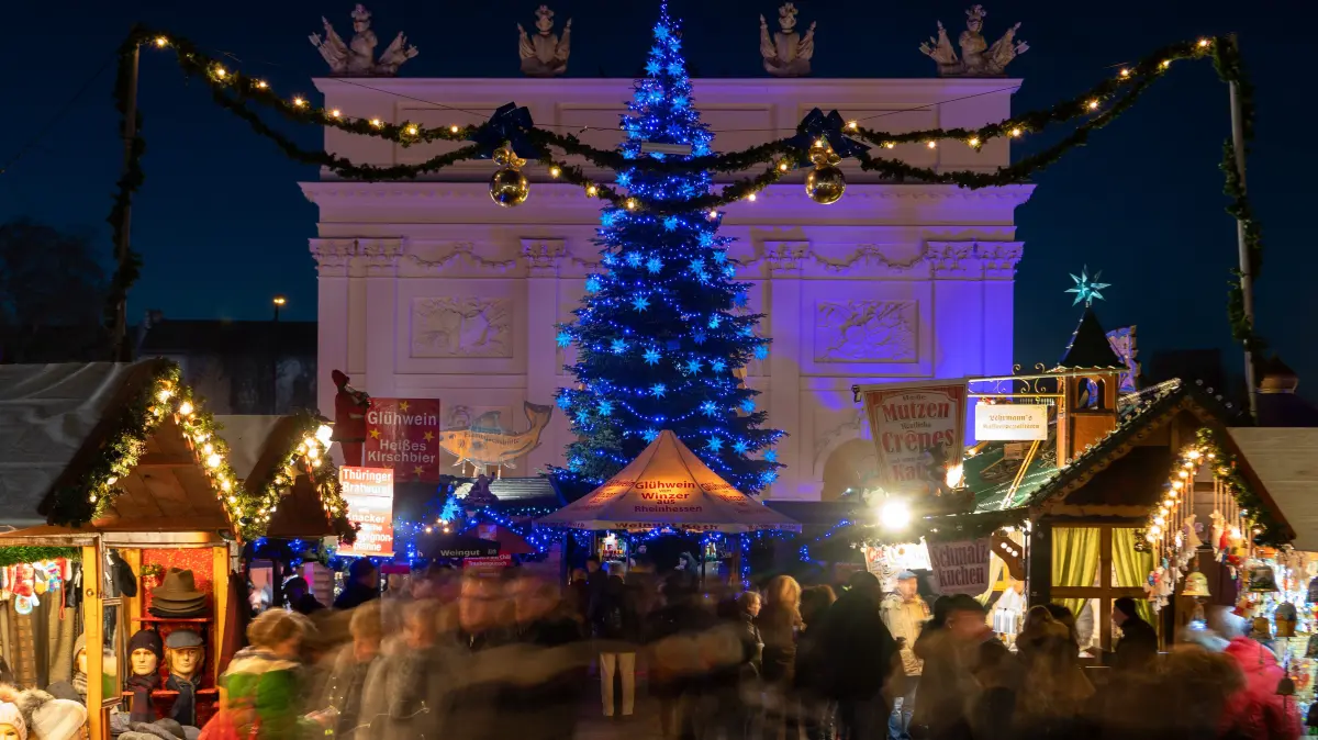Zahlreiche Besucher schlendern am Abend über den Weihnachtsmarkt "Blauer Lichterglanz" in der Brandenburger Straße vor der Kulisse des Brandenburger Tors in Potsdam. (zu dpa: «Weihnachtsmärkte mit höheren Preisen und weniger Beleuchtung») +++ dpa-Bildfunk +++