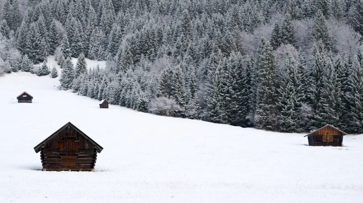Heuschober stehen auf einer schneebedeckten Wiese. +++ dpa-Bildfunk +++