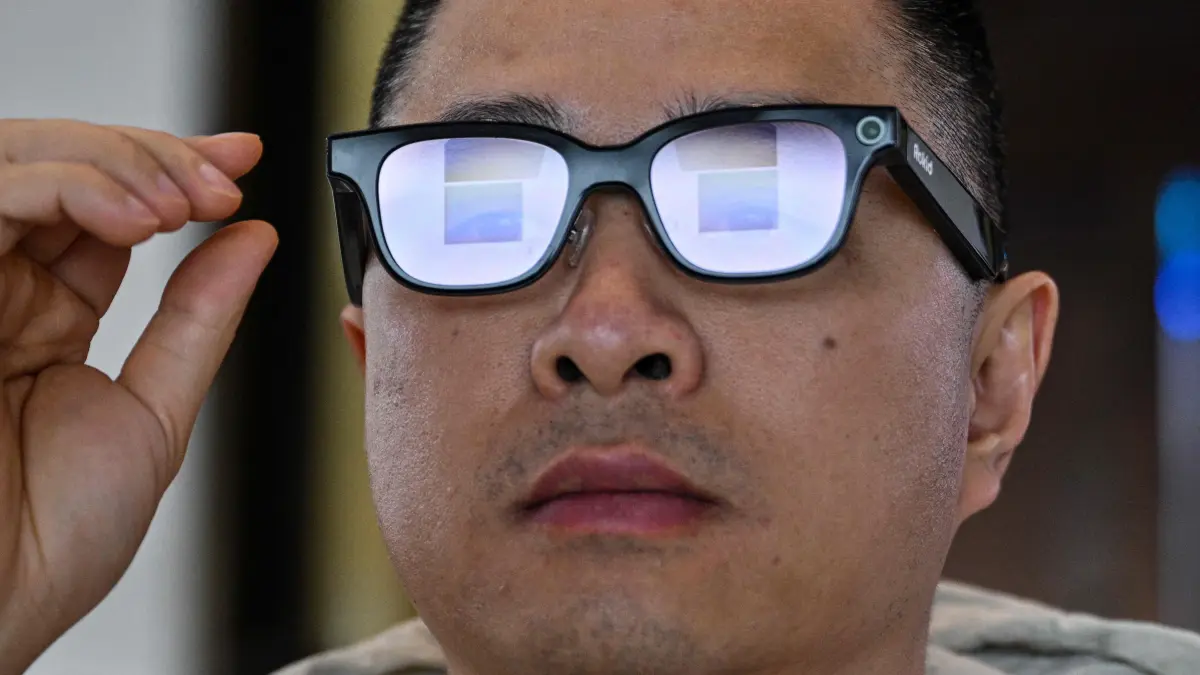 This picture taken on November 13, 2025 shows a man checking a pair of Rokid glasses with display and camera using artificial intelligence (AI) and augmented reality (AR) during a presentation event in Hangzhou, in China's eastern Zhejiang province. In China, AI glasses let the wearer pay in shops with just a glance at a QR code and a voice command, as a growing number of companies look to conquer both growing domestic and overseas markets. Interest in smart eyewear is soaring worldwide after more than a decade of stalled promise, with advances in artificial intelligence sparking renewed interest in the sector. (Photo by Hector RETAMAL / AFP) / To go with 'CHINA-TECHNOLOGY-WEARABLES-AI, FOCUS' by Emily WANG