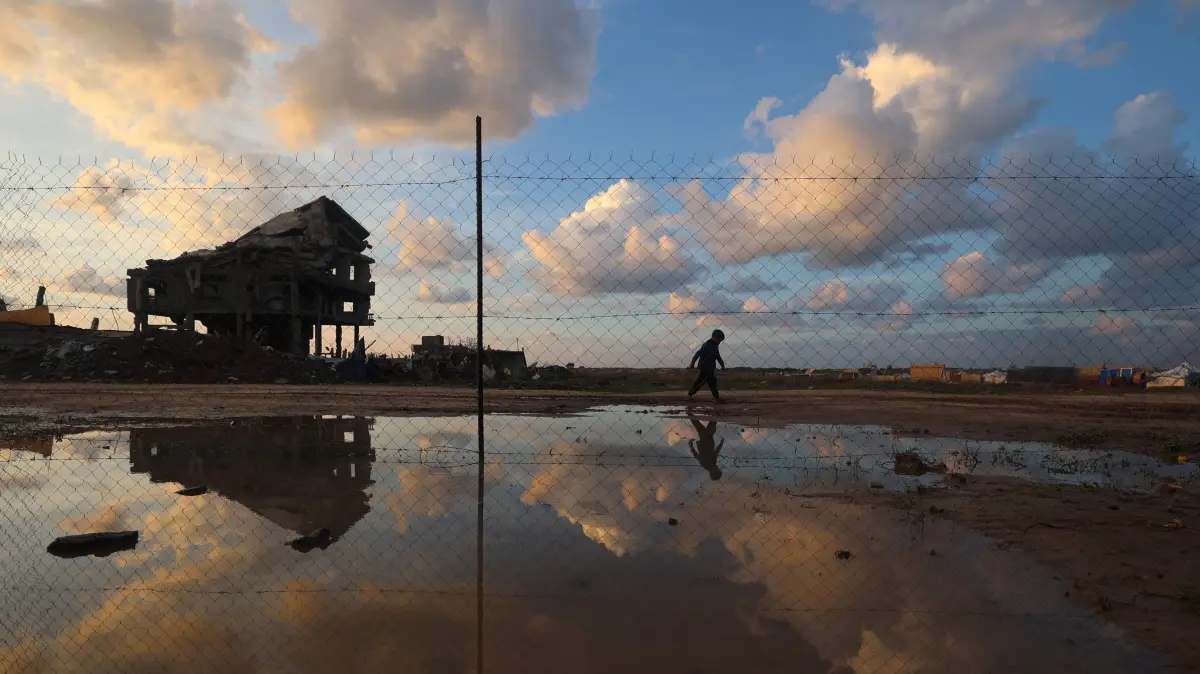 A Palestinian child walks past puddles of rain water in the Nuseirat refugee camp in the central Gaza Strip, on December 13, 2025. Gaza's civil defence agency on December 12, 2024, said at least 16 people had died in the last 24 hours, including three children who died from exposure to the cold, as a winter storm batters the territory. Heavy rain from Storm Byron has flooded tents and temporary shelters across the Gaza Strip, compounding the suffering of the territory's residents, nearly all of whom were displaced during more than two years of war. (Photo by Eyad Baba / AFP)