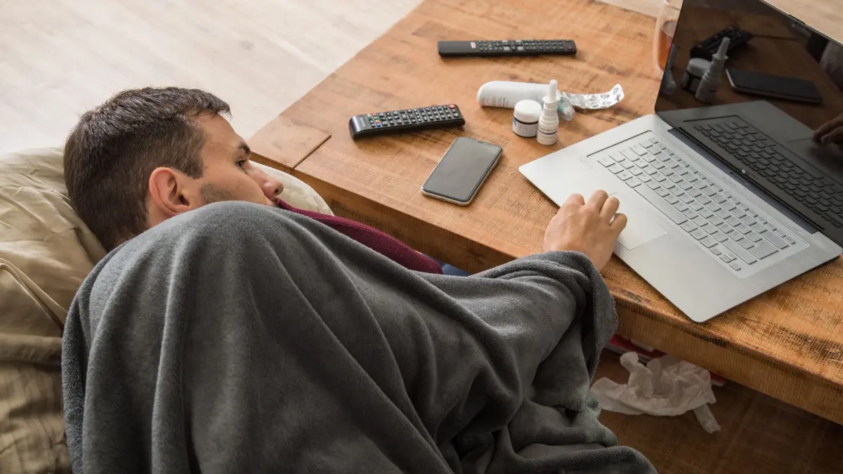 Ein Mann mit Erkältung bedient ein Laptop: ILLUSTRATION - Eine Kündigung während Krankheit trifft Arbeitnehmer hart. (zu dpa: «Darf ich während einer Krankschreibung gekündigt werden?») Foto: Christin Klose/dpa-tmn - Honorarfrei nur für Bezieher des dpa-Themendienstes +++ dpa-Themendienst +++