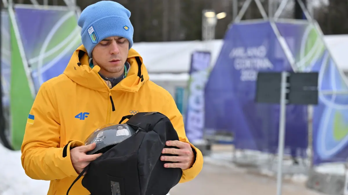 Olympische Winterspiele 2026: 12.02.2026, Italien, Cortina d'Ampezzo: Olympia, Olympische Winterspiele Mailand Cortina 2026, Skeleton, Männer, Wladislaw Heraskewytsch (Ukraine) hält seinen Helm und eine Tasche in den Händen. Im Streit um seinen Helm mit Bildern von im Krieg getöteten Sportkollegen ist der Ukrainer Wladislaw Heraskewytsch vom olympischen Skeleton-Wettbewerb ausgeschlossen worden. Foto: Robert Michael/dpa +++ dpa-Bildfunk +++