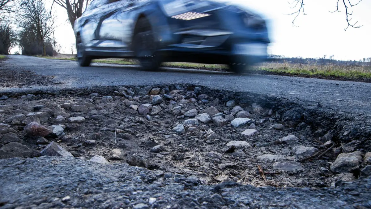 Auto fährt an einem Schlagloch vorbei: ARCHIV - Wer mit hohem Tempo durch ein Schlagloch fährt, riskiert Schäden an Lenkung, Radaufhängung, Reifen und Felgen. (zu dpa: «Schlagloch-Schäden am Auto: Wer zahlt?») Foto: Jens Büttner/dpa/dpa-tmn - Honorarfrei nur für Bezieher des dpa-Themendienstes +++ dpa-Themendienst +++