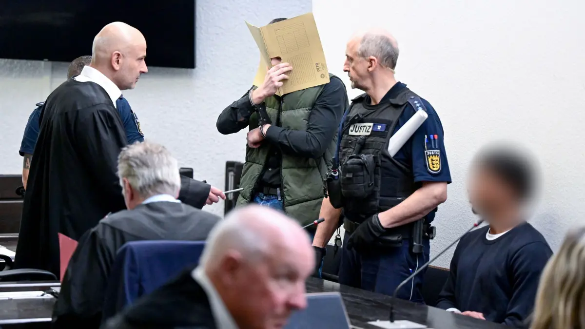 Beginn Prozess wegen versuchten Mordes: 13.03.2026, Baden-Württemberg, Stuttgart: Zwei Angeklagte stehen und sitzen im Gerichtssaal vor dem Beginn eines Prozess wegen versuchten Mordes und Vergewaltigung. Die vier Angeklagten sollen sich online als minderjährige Mädchen ausgegeben haben, um ahnungslose Männer bei fingierten Sextreffen in die Falle zu locken - und dann brutal zuzuschlagen. Foto: Bernd Weißbrod/dpa - ACHTUNG: Ein Angeklagter wurde(n) aus rechtlichen Gründen gepixelt +++ dpa-Bildfunk +++
