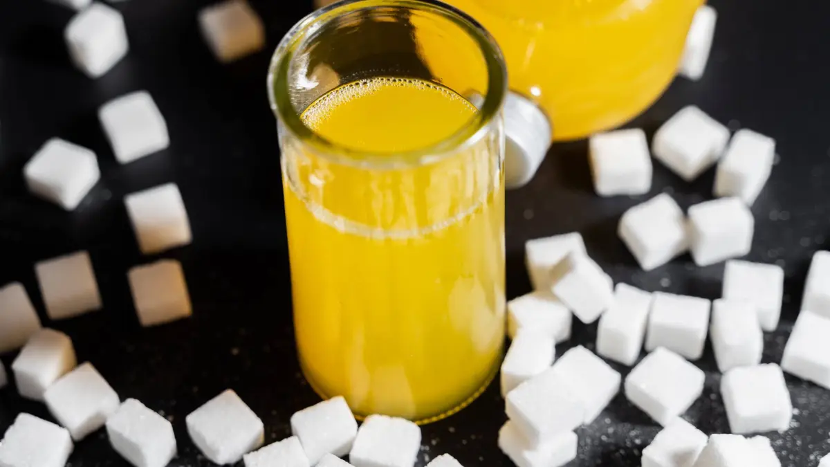 Germany - February 24, 2026: Glass and bottle of yellow lemonade surrounded by sugar cubes. Symbolic image of high sugar content, consumption and nutrition, stands for sugar tax, health debate and the link between sweet drinks and the risks of modern nutrition *** Glas und Flasche mit gelber Limonade, umgeben von Würfelzucker. Symbolbild hoher Zuckergehalt, Konsum und Ernährung, steht für Zuckersteuer, Gesundheitsdebatte und die Verbindung zwischen süßen Getränken und Risiken moderner Ernährung