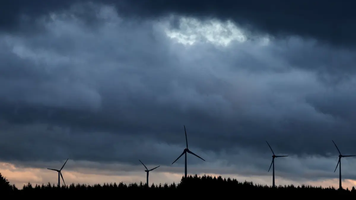 Windräder in Bayern: ARCHIV - 01.08.2023, Bayern, Aitrang: Windräder stehen bei Aitrang im Allgäu unter dichten Regenwolken hinter einem Wald. (zu dpa: «Erörterung zu Prestige-Windpark Altötting - Bühne für Bürger») Foto: Karl-Josef Hildenbrand/dpa +++ dpa-Bildfunk +++