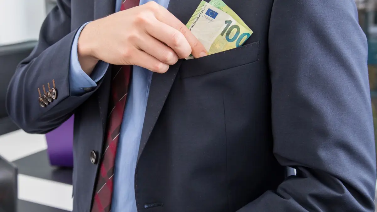 Ein Mann steckt sich einen 100 Euro Geldschein in die Tasche: ILLUSTRATION - Geld gegen Vorteilsgewährung? Das steht unter Strafe. (zu dpa: «Zwischen Gefallen und Gesetz: Wie erkenne ich Korruption?») Foto: Christin Klose/dpa-tmn - Honorarfrei nur für Bezieher des dpa-Themendienstes +++ dpa-Themendienst +++