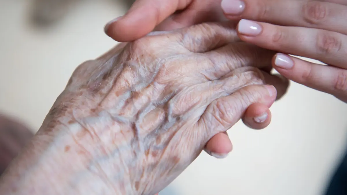 Pflegerin hält Hand einer Seniorenheim-Bewohnerin