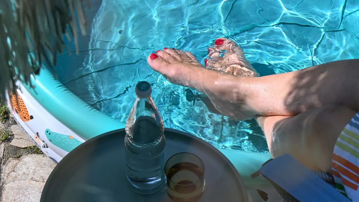 Sommerhitze - Urlaub auf der Terrasse: ARCHIV - 13.08.2025, Baden-Württemberg, Stuttgart: Eine Frau steckt bei sommerlicher Hitze auf einer Terrasse unter einem Sonnenschirm sitzend ihre Füße in ein Planschbecken mit kühlem Wasser.
Die Sommerferien wurden gar nicht zum Ausspannen erfunden. (zu dpa: «Wo die 30-Grad-Marke wieder geknackt wird») Foto: Bernd Weißbrod/dpa +++ dpa-Bildfunk +++