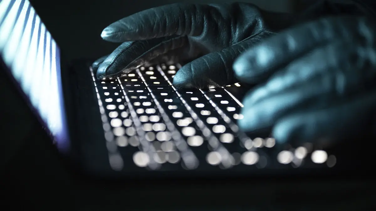 Eine Person tippt mit behandschuhten Händen auf einer beleuchteten Laptop-Tastatur. (Gestellte Szene) (zu dpa: «Ermittlungserfolg: Manche Cyber-Betrüger meiden Deutschland») +++ dpa-Bildfunk +++