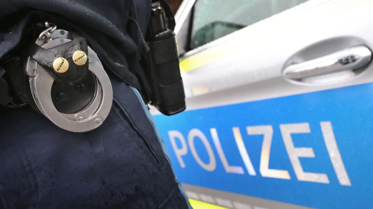 Polizei: ARCHIV - 15.03.2019, Bayern, Kempten: ILLUSTRATION - Ein Polizist mit Handschellen und einer Pistole am Gürtel steht vor einem Streifenwagen. (zu dpa: «Mann schießt in Gaststätte und auf Straße - U-Haft») Foto: Karl-Josef Hildenbrand/dpa +++ dpa-Bildfunk +++