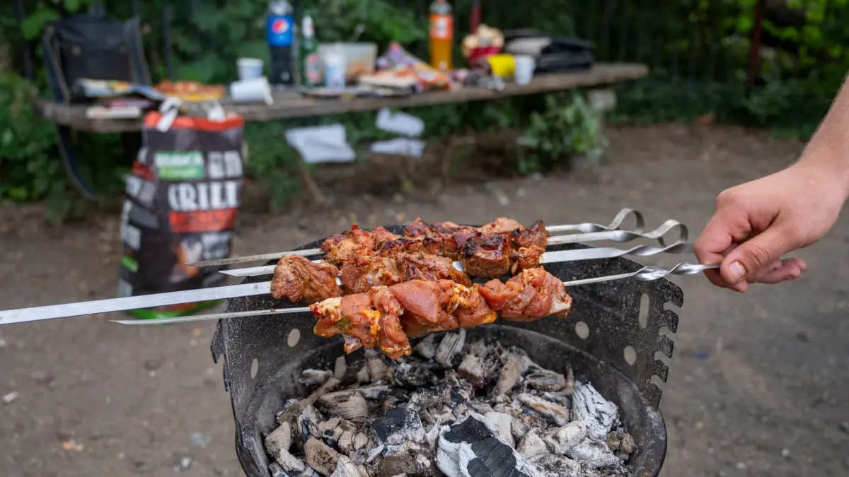 Grillen im Park: ARCHIV - 29.06.2022, Berlin: Ein Mann grillt im Volkspark Friedrichshain auf einem Grillplatz Fleischspieße. (zu dpa: «Grillwiese in Friedrichshain oft überfüllt - Mehr Flächen?») Foto: Christophe Gateau/dpa +++ dpa-Bildfunk +++