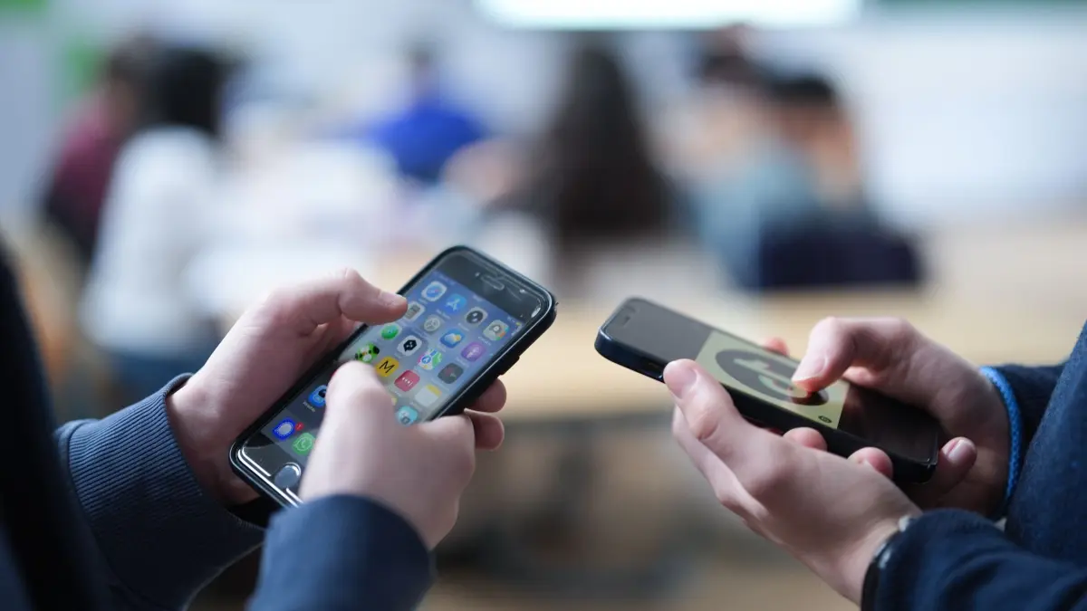 Aufklärung über Manosphere, Gewalt und toxische Männlichkeit: ILLUSTRATION - 13.02.2026, Hamburg: Zwei Schüler stehen in einem Klassenraum ab einem Gymnasium und schauen auf ihre Smartphones, auf einem der Displays ist das Logo der Social-Media-Plattform TikTok zu sehen. (zu dpa: «Wie TikTok toxische Männlichkeit bei Jugendlichen befeuert») Foto: Marcus Brandt/dpa +++ dpa-Bildfunk +++