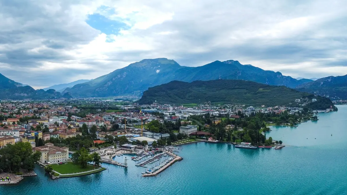 Das Panorama zeigt die Stadt Riva del Garda am nördlichen Ende des Gardasees, umgeben von majestätischen Bergen. Die Altstadt mit ihren charakteristischen, bunten Gebäuden erstreckt sich entlang des Ufers.
