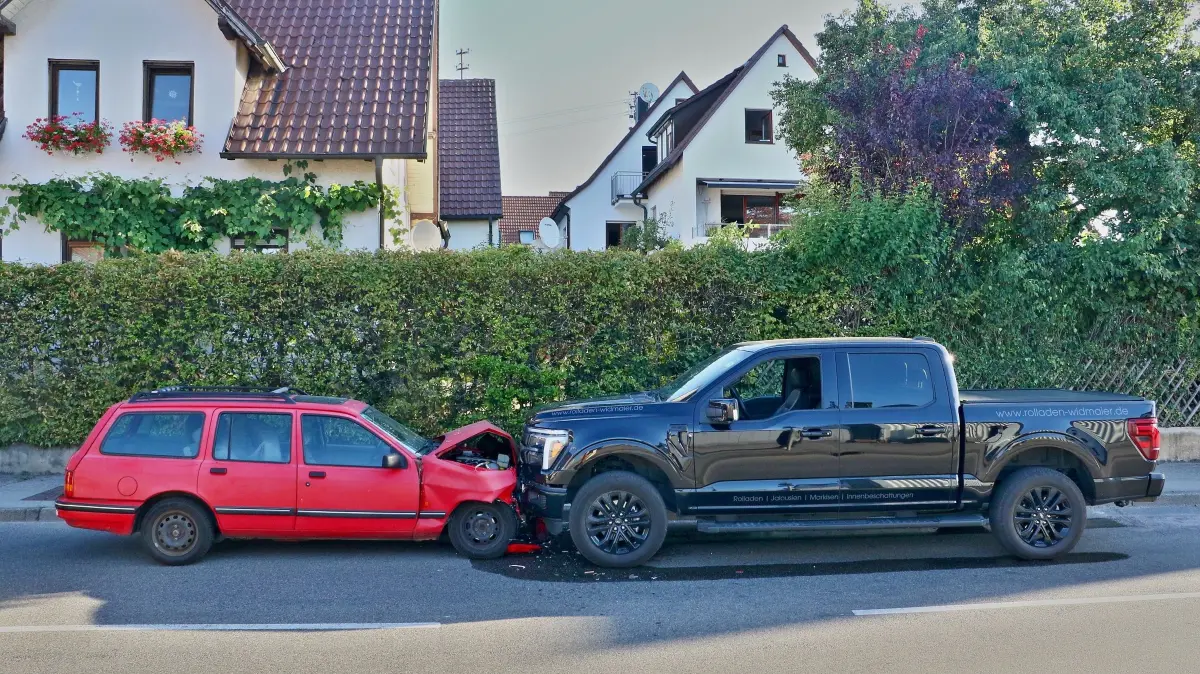 04.07.2026: Ein Frontalzusammenstoß mit ungleichen Vorausetzungen ereignete sich am Samstagmorgen in Leonberg-Höfingen. Kurz nach 7 Uhr befuhr der Lenker eines alten Ford Sierra (Bauzeitraum bis 1993, Leergewicht knapp 1200 kg) die Pforzheimer Straße in Richtung Ditzingen. Etwa in Höhe der Schillerstraße geriet das Fahrzeug auf die Gegenspur. Dort fuhr zu diesem Zeitpunkt der Fahrer eines Ford F150 Pickup (Leergewicht über 2200 kg) in Richtung Ortmitte. Zwar konnte der Fahrer des riesigen Geländewagens nach eigenen Angaben noch abbremsen, der Sierra prallte denoch wuchtig gegen die hochaufragende Front des Pickup. Da nicht klar war, ob der Fahrer des Ford Sierra sein Fahrzeug eigenständig verlassen kann alarmierte die Leitstelle neben Rettungsdienst und Polizei auch die Freiwillige Feuerwehr Leonberg mit den Abteilungen Innenstadt und Höfingen. Der Fahrer konnte jedoch vom ersteintreffenden Rettungsdienst aus seinem schwer beschädigten Pkw gerettet und in ein Krankenhaus transportiert werden. Den zweiten "Insassen" des Sierra rettete dann die Feuerwehr aus dem Kofferraum. Dort befand sich eine Hundetransportbox, der Hund darin hatte den Unfall zwar körperlich unversehrt überstanden, reagierte jedoch äußerst unentspannt auf jegliche Annäherung. Aus diesem Grund wurde die Box etwas abseits auf dem Gehweg gelagert und der Hund möglichst ungestört gelassen. Nachdem die ausgelaufenen Betriebsmittel abgestreut waren konnte die Feuerwehr Einsatzstelle und Hund an die Polizei zur weiteren Versorgung übergeben.
Foto: KS-Images.de/Andreas Rometsch