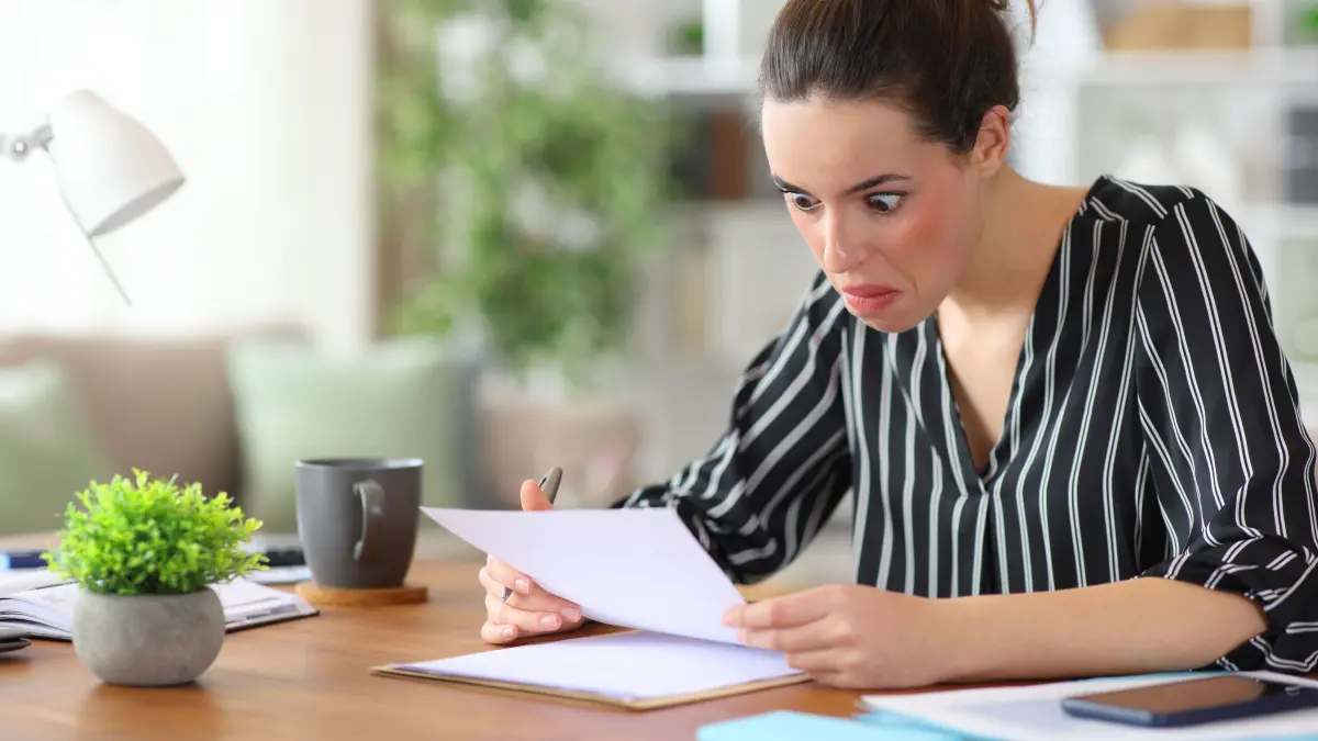 Perplexed self employed reading paper document in a wooden dekstop working at home