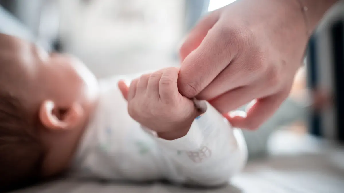 Ein Baby klammert sich an den Finger seiner Mutter.