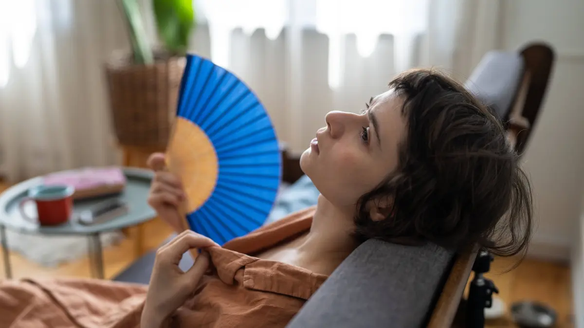 Eine traurige Frau, die zu Hause die Sommerhitze erträgt, sitzt auf dem Sofa, atmet kaum noch und fächelt sich mit einem Papierfächer Luft zu. Sad exhausted woman enduring summer heatwave at home, sitting on couch hardly breathing and waving paper fan, unwell worried female struggling with heat while resting on sofa fanning herself with fan. LicenseRF ,model released, Symbolfoto Copyright: xZoonar.com/DmitriixMarchenkox 24979772 ,model released, Symbolfoto ,property released