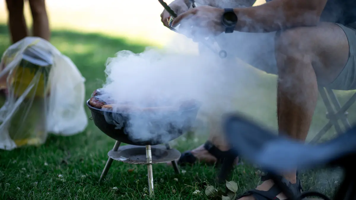 So bitte nicht! Ein Mann sitzt im Park vor einem rauchenden Grill.