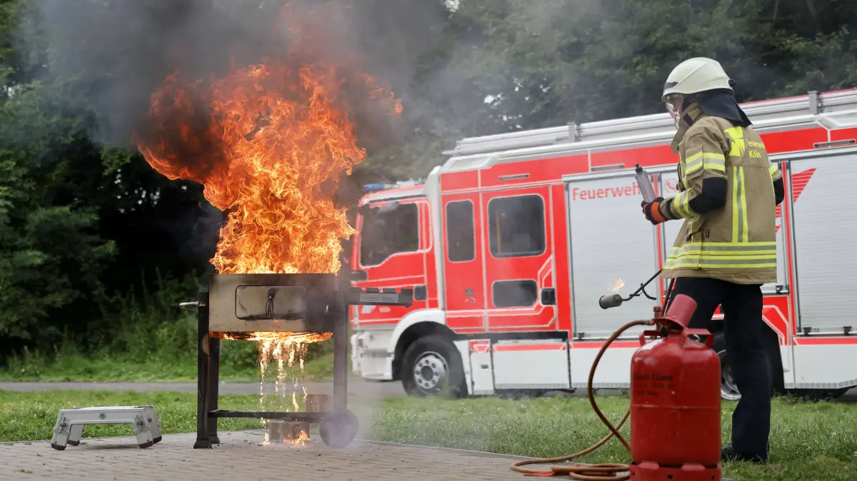 Ein Feuerwehrmann zeigt Stichflammen durch Brandbeschleuniger am Grill. Die Feuerwehr Köln demonstriert Gefahren beim Grillen, da es jährlich mehrere Tausend Grillunfälle in Deutschland zu beklagen gibt.