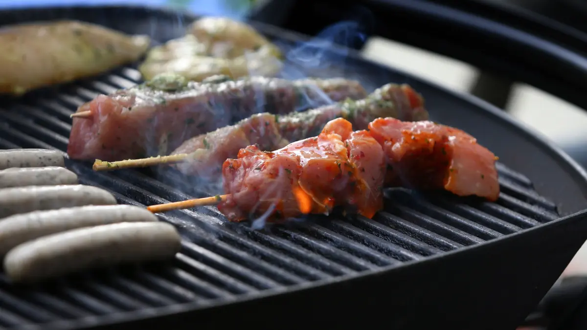 Fleischspieße, Bratwürste und Steaks liegen auf dem Rost eines Gasgrills.