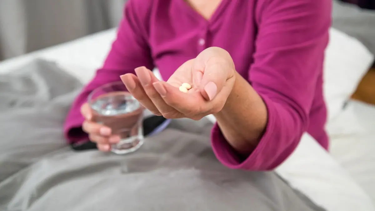 Eine Frau nimmt ein Medikament im Bett ein: ILLUSTRATION - Eine Hormonersatztherapie kann Hitzewallungen - und auch andere wechseljahresbedingte Beschwerden - lindern. (zu dpa: «Wechseljahre: Was hilft gegen die nervigen Hitzewallungen?») Foto: Christin Klose/dpa-tmn - Honorarfrei nur für Bezieher des dpa-Themendienstes +++ dpa-Themendienst +++