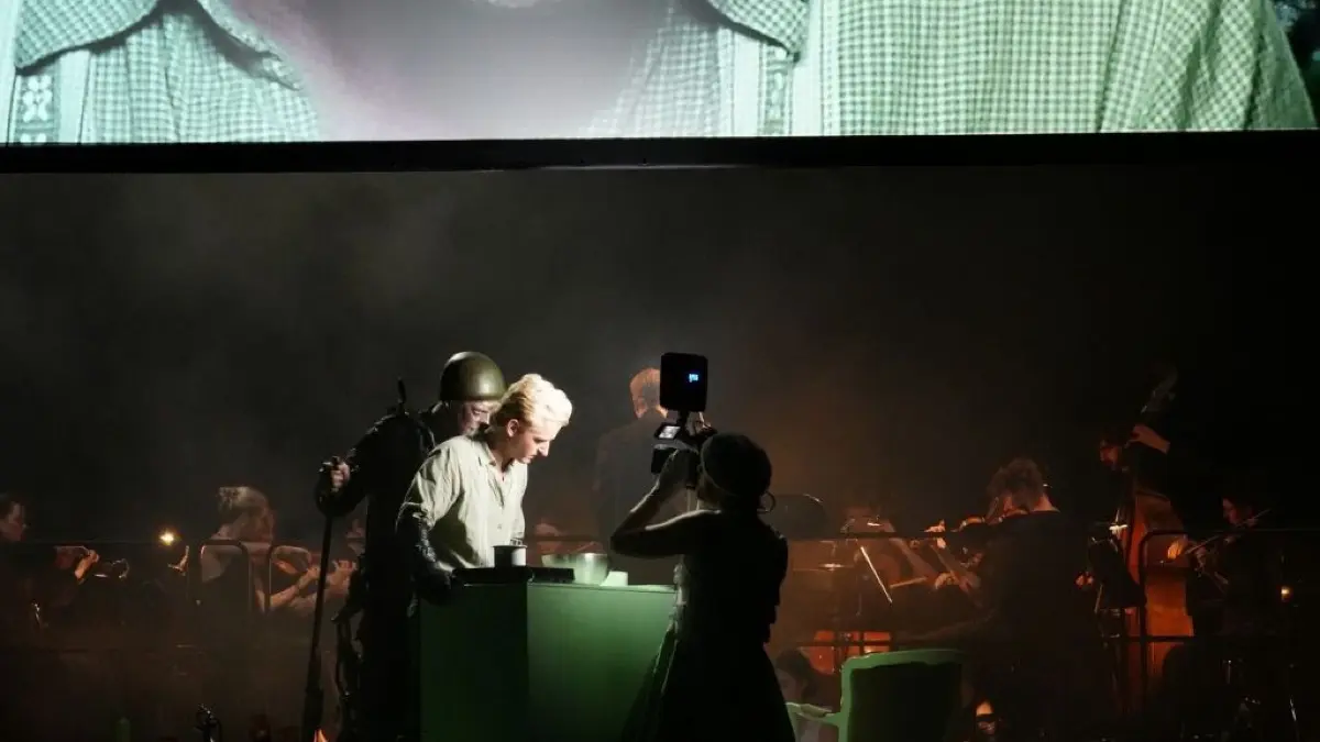 Die Inszenierung beinhaltet auch moderne Stilmittel, wie zum Beispiel eine Live-Übertragung auf einen großen Bildschirm, der Teil des Bühnenbilds wird.