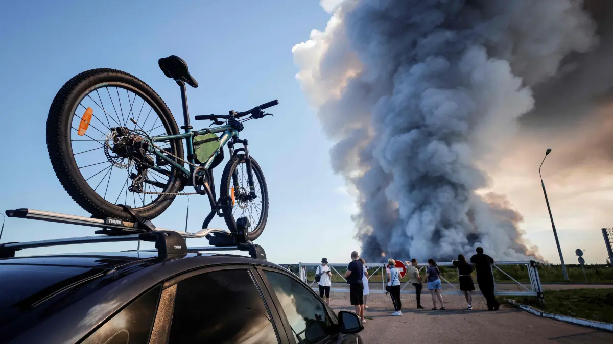 RUSSIA-UKRAINE-CONFLICT-ATTACKS: Bystanders watch as smoke rises from a fire at the Russian e-commerce firm Wildberries' logistics complexes in the town of Elektrostal outside Moscow on July 18, 2026. A Ukrainian drone attack on two logistics centres in Russia killed eight people and injured 24, officials said on July 18, 2026, when the Moscow region reported a new wave of drone strikes. Russian e-commerce firm Wildberries said its logistics complexes in Kotovsk and Elektrostal, in the Tambov and Moscow regions respectively, came under attack. One person was killed and 37 were injured at the Elektrostal warehouse, according to the region's governor, Andrei Vorobyov. (Photo by TATYANA MAKEYEVA / AFP)