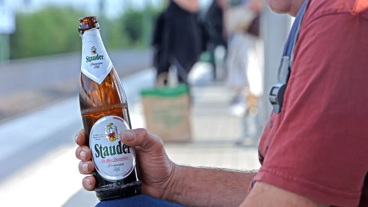 Ein Mann hält an einem Bahnsteig sein Feierabendbier in der Hand und wartet auf den Zug.