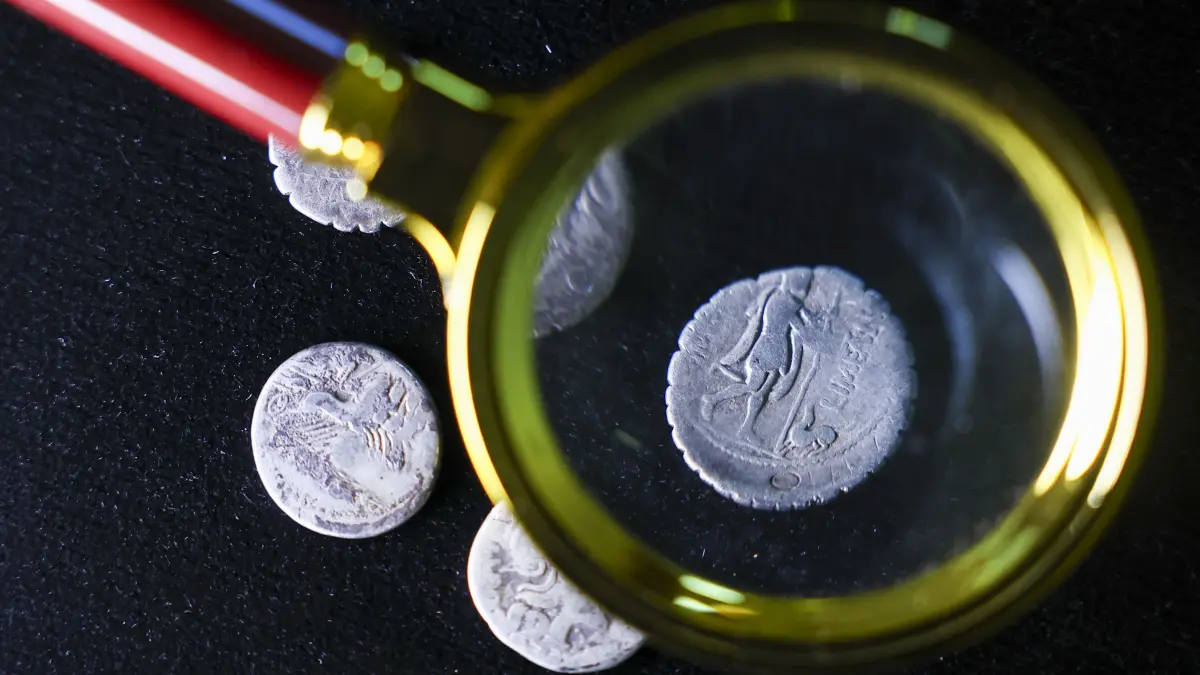 Eine Numismatikerin (Münzforscherin) untersucht eine über 2000 Jahre alte Silbermünze mit dem Abbild des heimkehrenden Odysseus mit Wanderstab, der von seinem Hund Argos begrüßt wird, im Landesmuseum für Vorgeschichte. Bei einem außergewöhnlichen Hortfund wurden erstmals in Sachsen-Anhalt fünf dieser Silberdenare der Römischen Republik entdeckt. Unter der Lupe sieht man: Die uralte Silbermünze zeigt einen Mann und einen Hund..