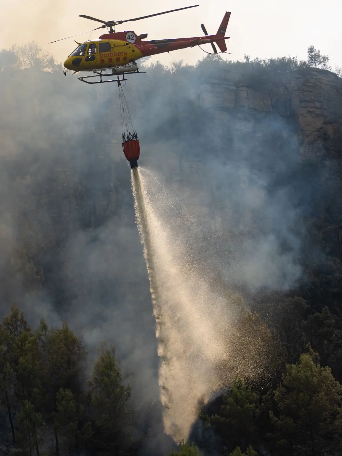 Ein Löschhubschrauber ist in Cervelló während eines Waldbrandes im Einsatz. Die Zivilschutzbehörde hat die Evakuierung von rund 300 Menschen aus den Wohnsiedlungen Can Paulet und Les Rovires in Cervelló angeordnet.