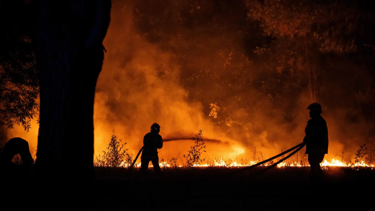 FRANCE-WILDFIRE-ENVIRONMENT: Firefighters spray water on a burning forest close to a residential area during a wildfire near Lege-Cap-Ferret, southwestern France, on July 23, 2026. A highly virulent wildfire has swept through more than 3700 hectares since July 22, 2026 near the Arcachon Basin (Gironde), where nearly 20,000 residents and tourists have been evacuated in total from this area of the Landes de Gascogne forest, already devastated by flames in 2022. (Photo by JULIEN DE ROSA / AFP)