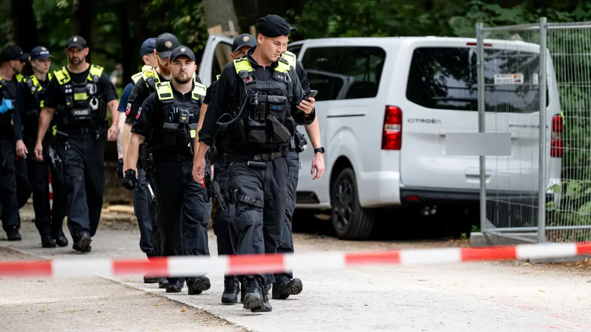 Auto fährt in Menschenmenge - CSD abgebrochen: 26.07.2026, Berlin: Polizisten laufen an einem Wagen, der in einen Baum gefahren ist an. Am Rande des Christopher Street Day in Berlin war das Fahrzeug in eine Menschenmenge gefahren. Dabei wurde eine Frau getötet, 16 weitere Menschen verletzt, zum Teil schwer. (zu dpa: «Mutmaßlicher Täter nach CSD-Anschlag getötet») Foto: Fabian Sommer/dpa +++ dpa-Bildfunk +++
