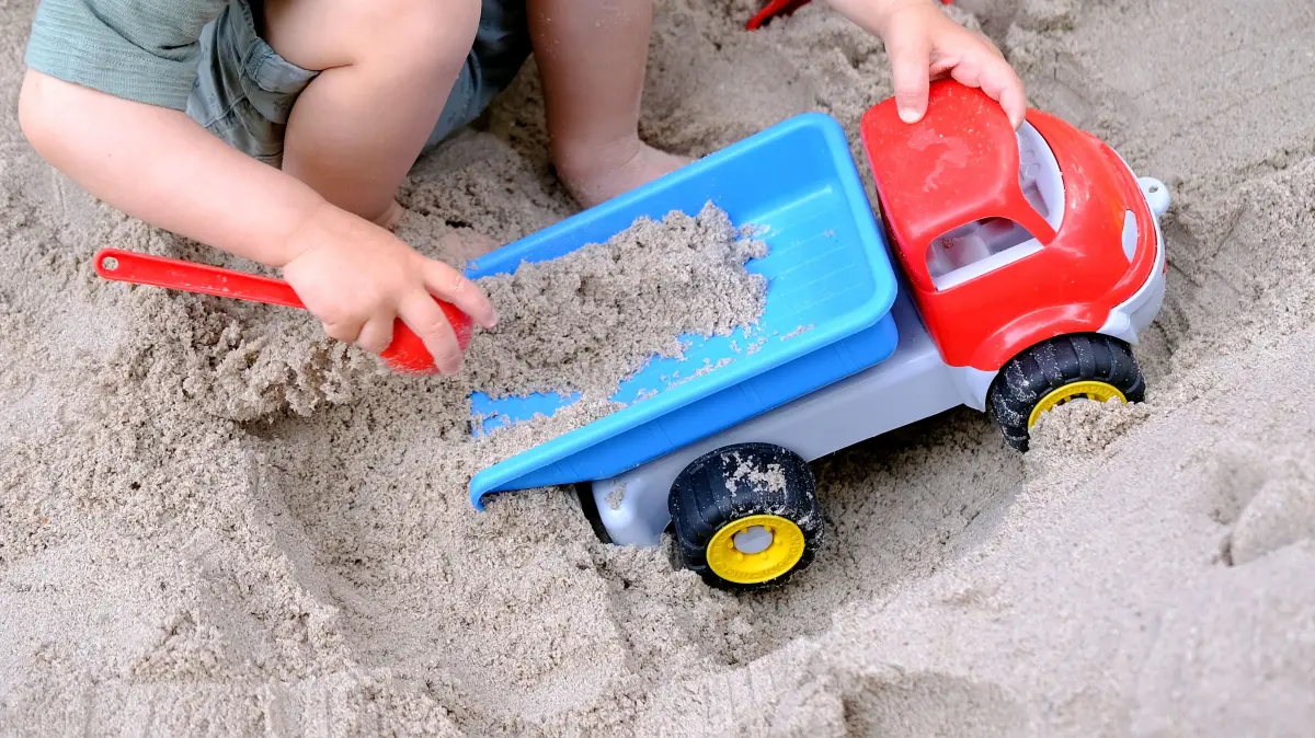 Ein Kleinkind spielt mit einem Spielzeugkipper und einer Schaufel in einem Sandkasten. (zu dpa: «Saarland prüft vollständige Kita-Pflicht – Hürden bleiben») +++ dpa-Bildfunk +++